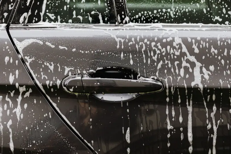 Snow foam running down a dark car door during an exterior wash